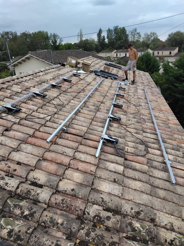 Homme sur un toit avec des barres métalliques installées sur des tuiles.